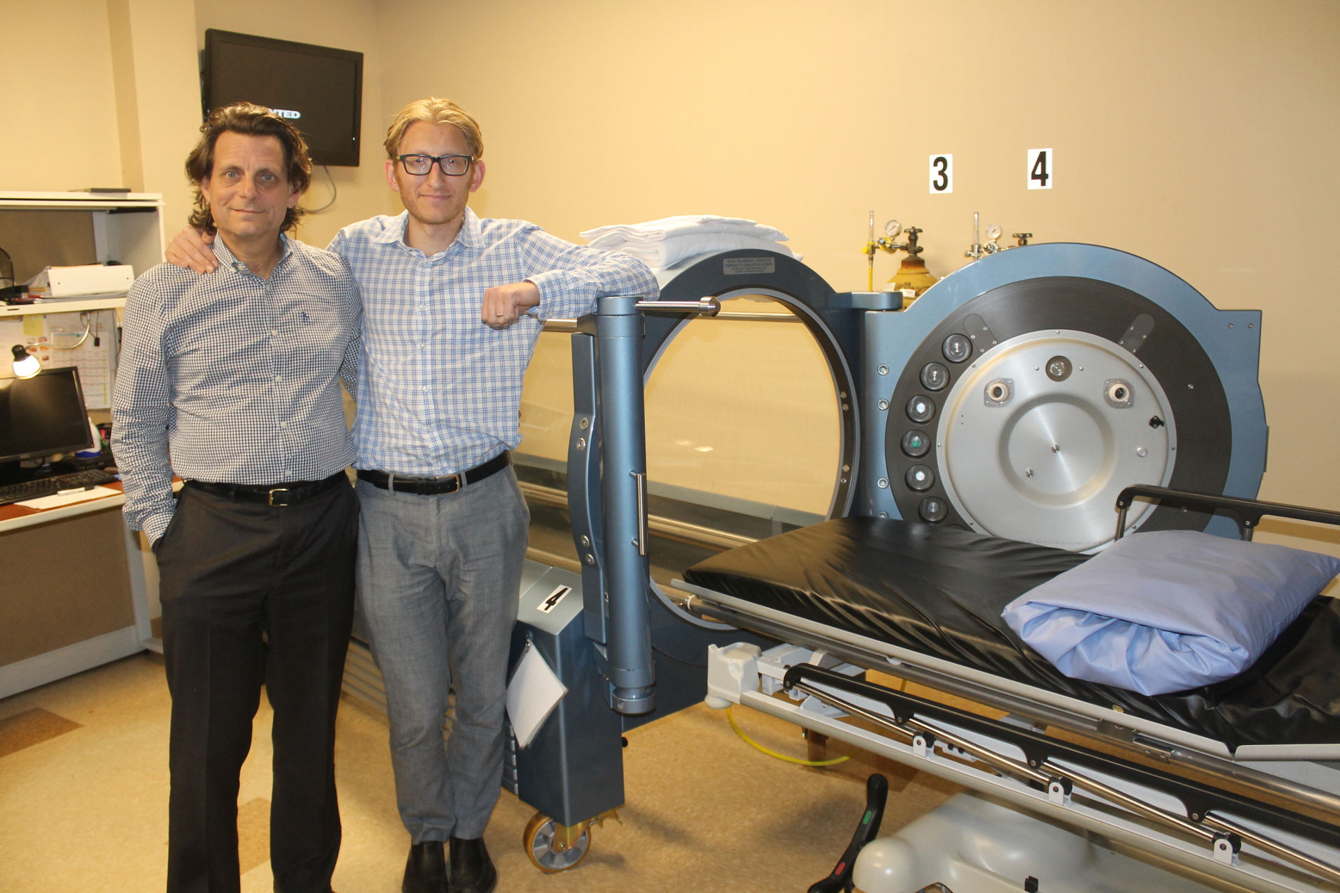 Doctors Alan (L) and Scott Sherr (R) stand next to a hyperbaric oxygen chamber at Hyperbaric Medical Solutions in Woodbury. (Rashed Mian/Long Island Press) 