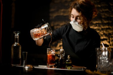 young woman at bar accurate pours cold cocktail into glass.