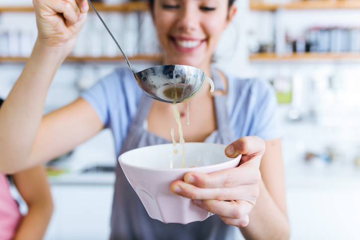 Young woman serving vegetable soup in the kitchen.