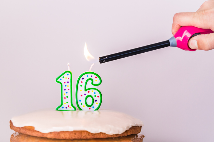 Man’s hand lighting sixteenth birthday candles on rustic vanilla layer cake