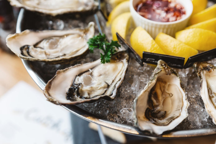 Close up Fresh Oysters and many kinds of fresh oysters served in round tray with slice lemon and spicy sauce.