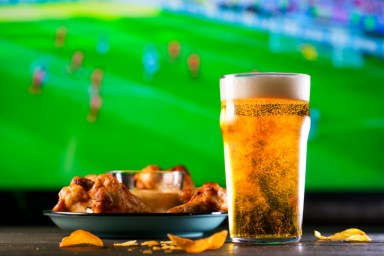 A glass of beer and hot chicken wings on a dark wooden table with crushed potato chips