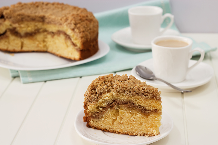 Close-up piece of homemade Cinnamon crumble coffee cake and cup of milk tea. White wooden background.