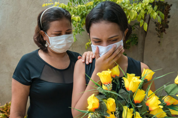 Woman mourning, wearing black and holding flowers, someone puts a hand on her to console funeral