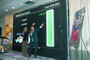 Auctioneer Elyse Luray  and David Miller show  the $200,000 raised to  send children to camp.