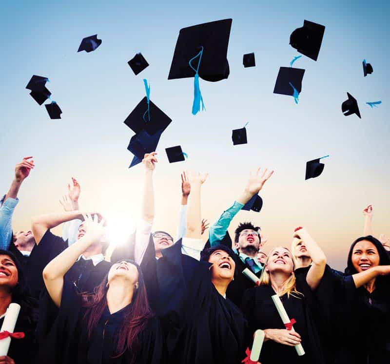 Smiling students throwing graduation caps in air