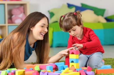 Mother and daughter playing together with colorful construction toys on a carpet on the floor af a bedroom at home teen babysitting