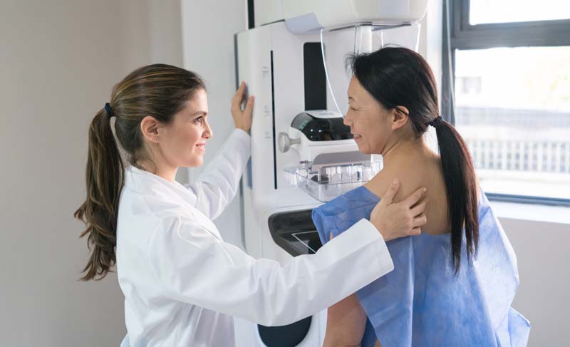 Female gynecologist helping a patinet get in posicion for a mammogram