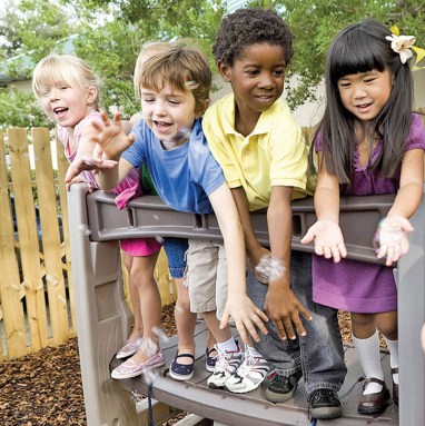 Preschool children playing on playground with teacher