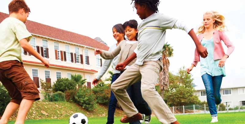 Energetic school children playing football, outdoors