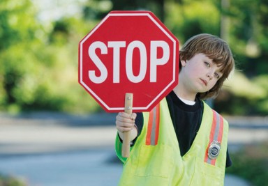 Portrait of a young boy crossing guard standing on the road holding a stop sign
