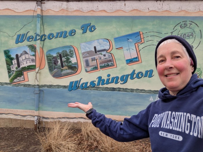 Librarian Rachel Fox poses next to a Welcome to Port Washington sign while on a walk