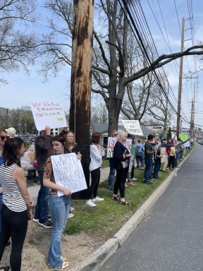 People gathered outside a Tesla dealership in Manhasset to protest against the actions of the president's administration on the 250th anniversary of the start of the Revolutionary War