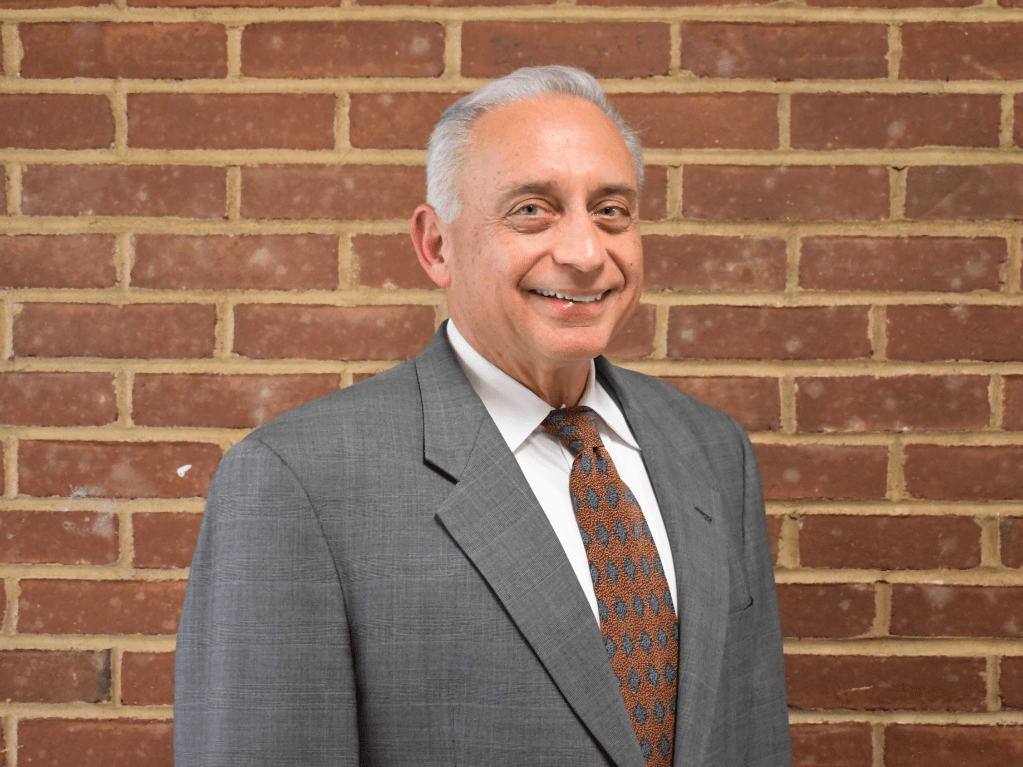 Carle Place board president stands in front of brick wall.