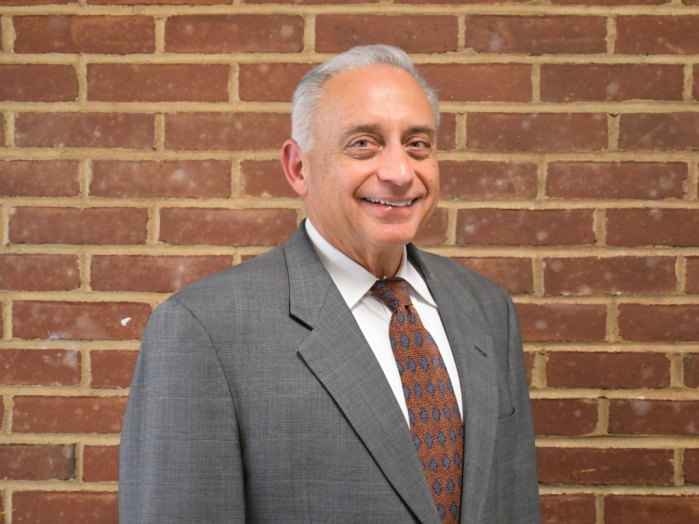 Carle Place board president stands in front of brick wall.