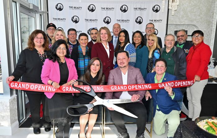A group of people stand in front of a red ribbon with scissors to celebrate The Beauty Cellar opening.