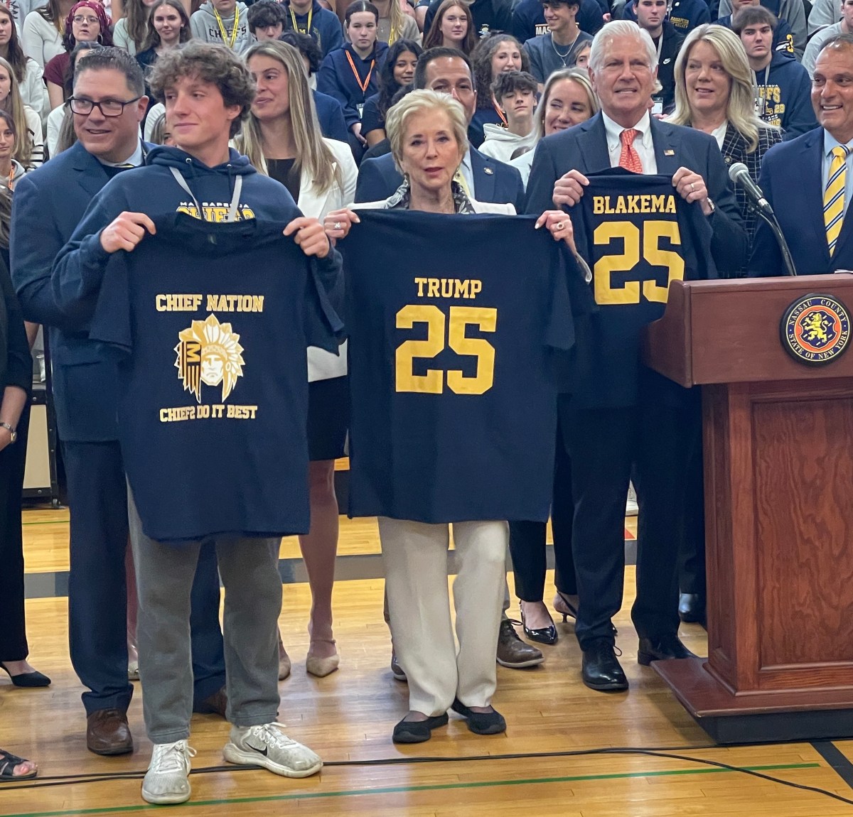 A Massapequa High School senior, the head of the U.S. Department of. Education, Linda McMahon and Nassau County Executive Bruce Blakeman (L. to R.) with Massapequa Chiefs shirts