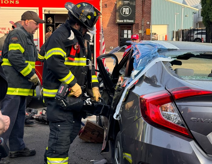 Firefighters take turns removing the door to a sedan using a handheld cutter tool.