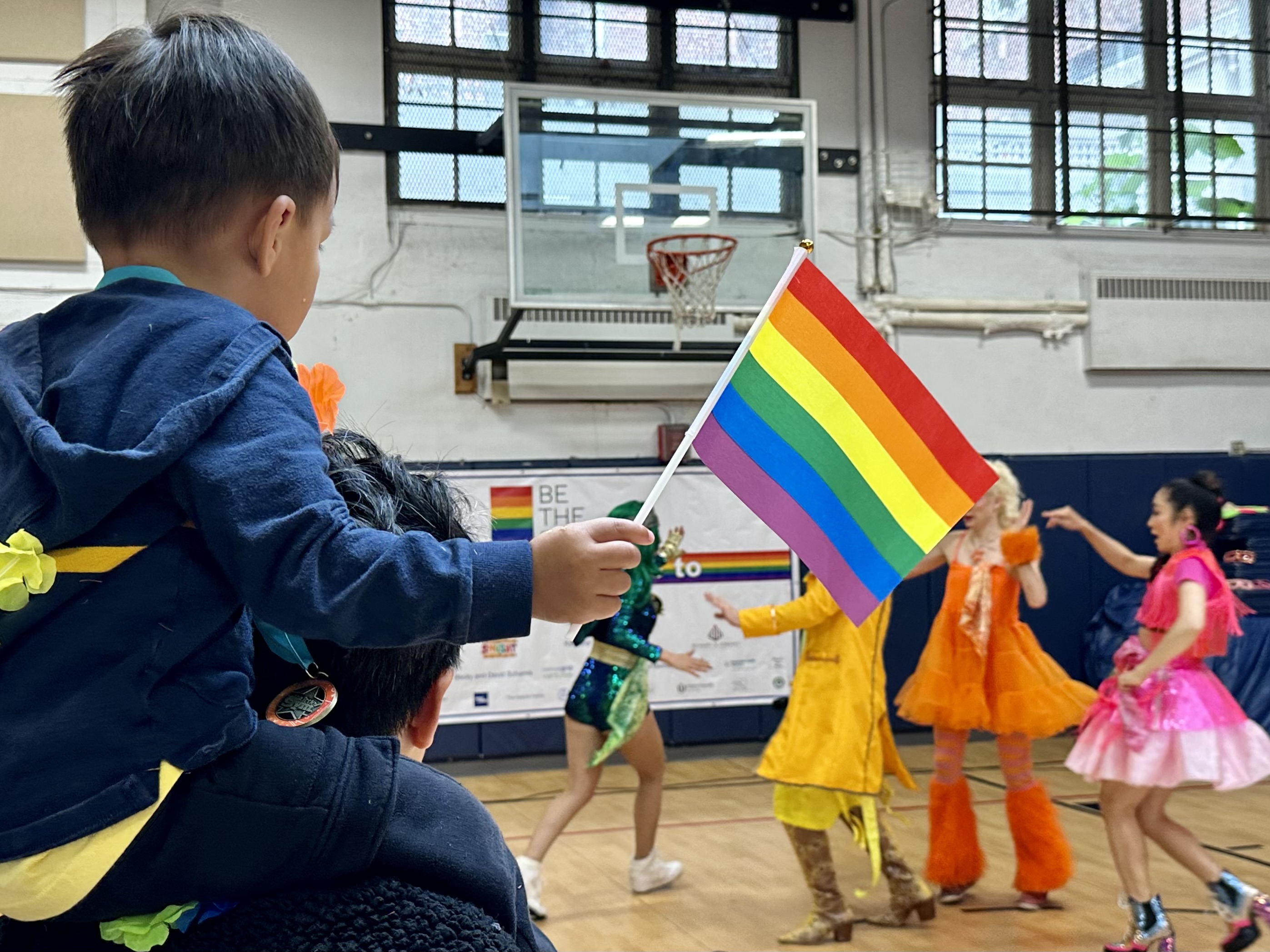 A child waves a Pride flag while sitting on their parent's shoulders.