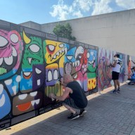 Muralists paint a construction fence on Main Street.