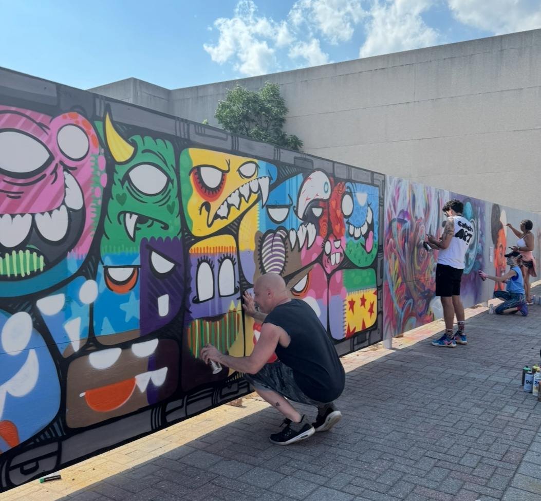 Muralists paint a construction fence on Main Street.