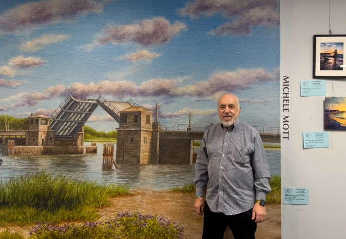 Bayville Arts Council Chair Philip Pecorino stands in front of a mural of the Bayville Bridge by Michelle Mott.