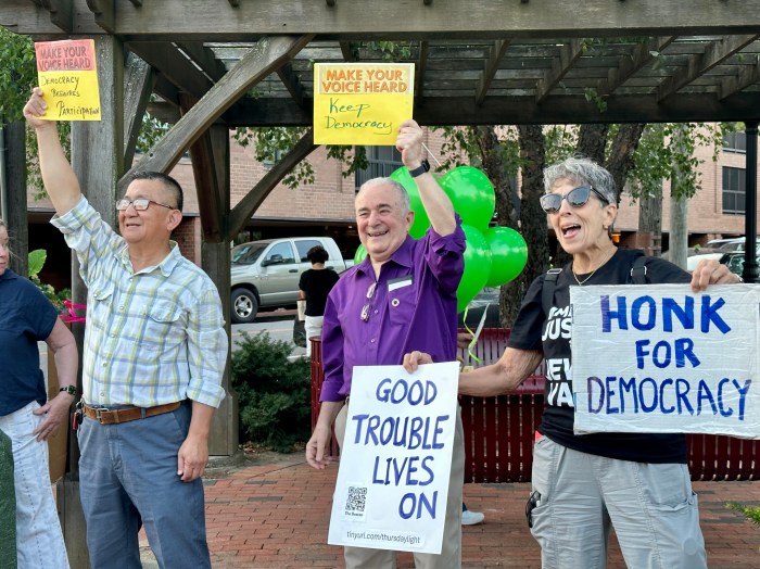 Demonstrators Charles Chiu, Ronald Gross and Nina Gordon (L. to R.) wave signs at the vigil in Great Neck.