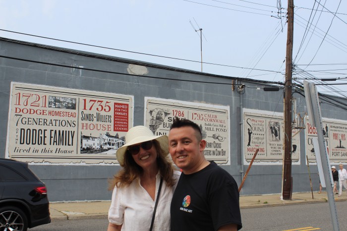 Diane Luger (L.) and Jason Diaz (R.) in front of their mural on the historDiane Luger (L.), who designed the mural, and Jason Diaz (R.), who painted it, stand in front of their work depicting the history of Port Washington.y of Port Washington.
