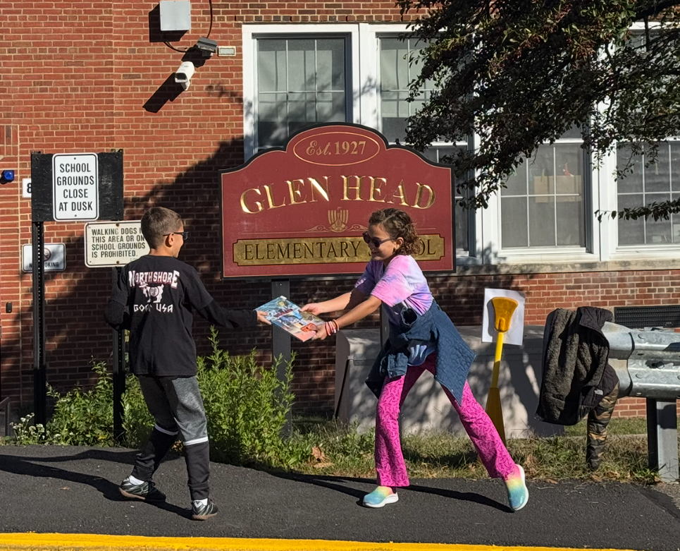 Third grade students pass books to one another in front of Glen Head Elementary School.