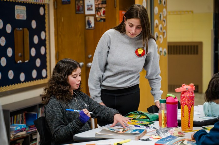 A high school student connects with a younger student, talking with her about the puzzle she is decorating.