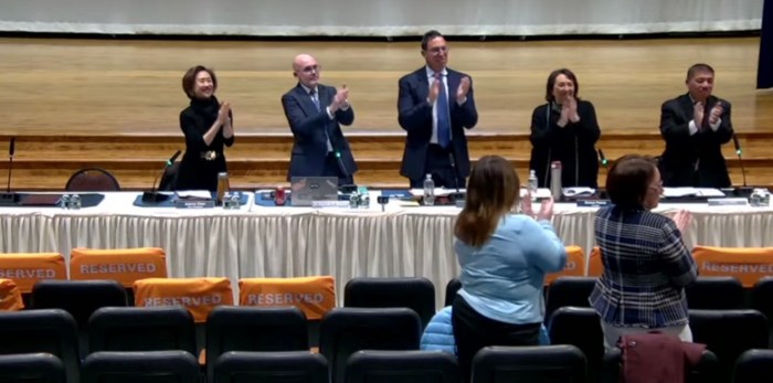 The school board stood and applauded as the new interim principal of E.M. Baker School, Heather Sweet-Lazos, walked to the podium.