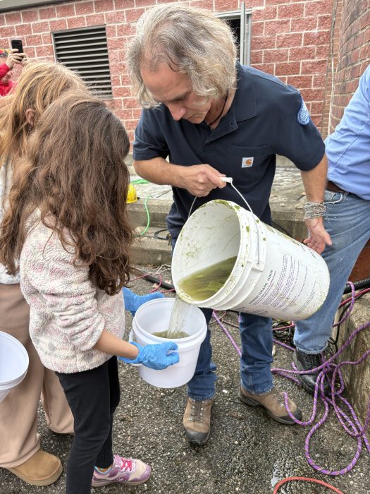 Port Washington Water Pollution Control District Superintendent Windsor Kinney pouring frogs/fish into a child's bucket to send them back to the pond.