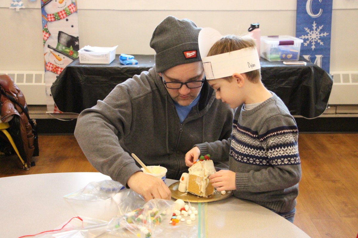 A teacher helping a child frost a gingerbread house at Heights School.