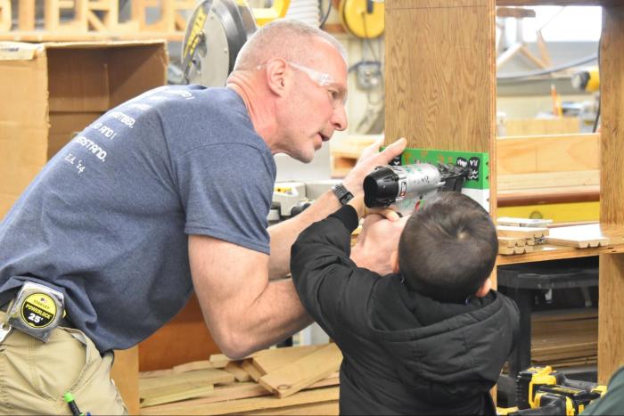Safety comes first as Farmingdale High School technology teacher Corey Sterler mentors a young builder on proper tool handling.