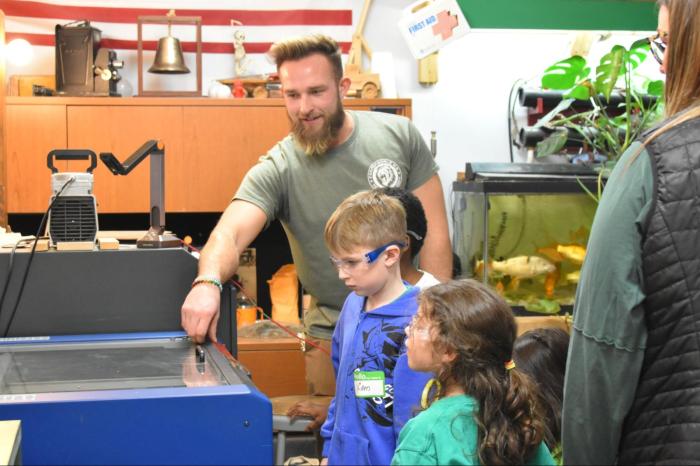 Innovation takes center stage as Farmingdale High School Technology Teacher Matthew Hobbes demonstrates how the engraving machine personalizes the project.