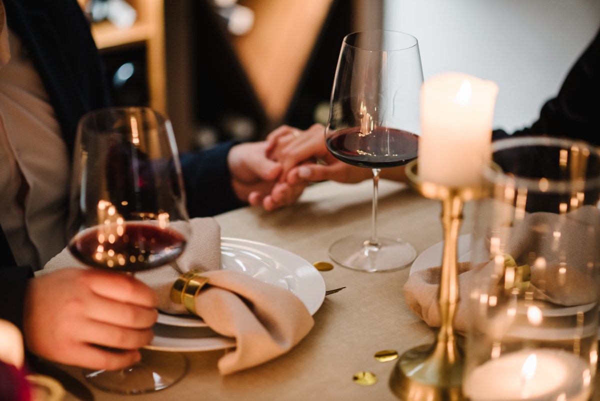 Romantic date by candlelight at night. Proposal hand and heart. Hands man and woman hold glasses at home. Toast. Couple in love drinking wine. Cheers. Dinner setup table for couple on Valentine’s day.