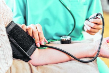 Female doctor measuring blood pressure of senior woman at home